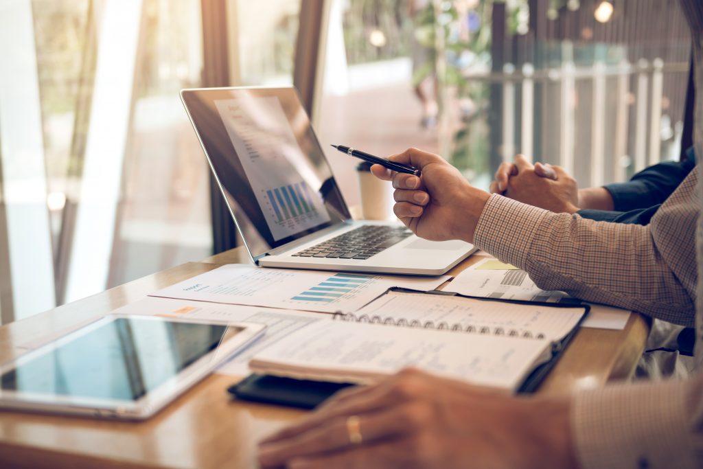 Business partnership pointing to the graph of the company financial statements report and profits earned during in the computer screen with giving a presentation to colleagues in office room.